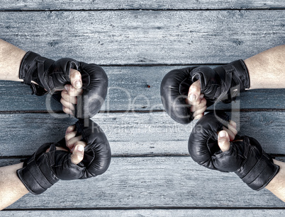 Two pairs of human hands in black leather boxing gloves facing e
