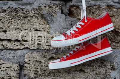 Youth red sneakers with laces hanging on a brick wall background