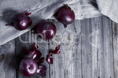Four red onions on the gray wooden surface