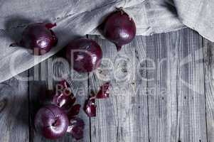 Four red onions on the gray wooden surface
