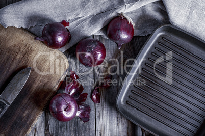 black frying pan and a red onion on a gray wooden surface