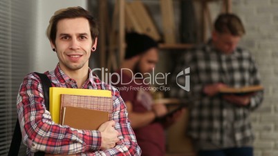 Smiling hipster student holding books at library