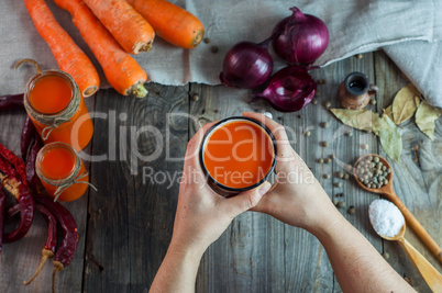 Two female hands holding an iron mug with carrot juice