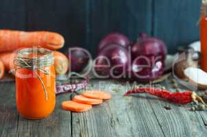 Carrot fresh juice in a glass container among the vegetables