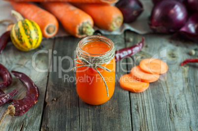 Carrot juice in a transparent little jar among the fresh vegetab