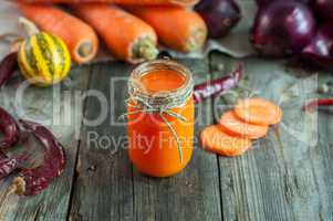 Carrot juice in a transparent little jar among the fresh vegetab