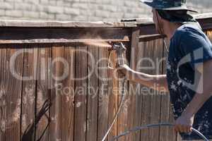 Professional Painter Spraying Yard Fence with Stain