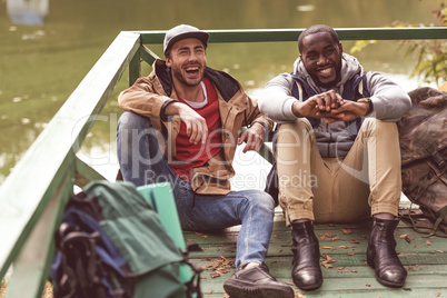 Young men with backpacks sitting on pier