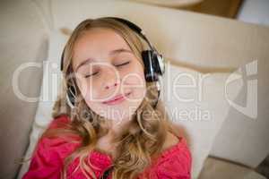 Cute girl lying on sofa and listening to music on headphones in living room