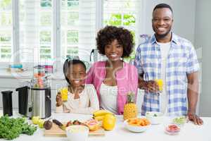 Smiling parents and daughter having a glass of orange juice in kitchen