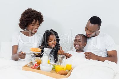 Smiling parents and kids having breakfast in bedroom