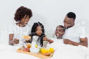 Smiling parents and kids having breakfast in bedroom