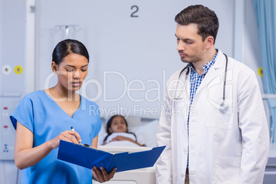 Nurse and doctor discussing over clipboard