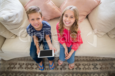 Smiling siblings sitting on sofa with digital tablet in living room