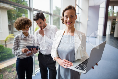 Businesswoman holding laptop while colleagues discussing over digital tablet Businesswoman holding laptop while colleagues discussing over digital tablet