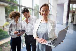 Businesswoman holding laptop while colleagues discussing over digital tablet