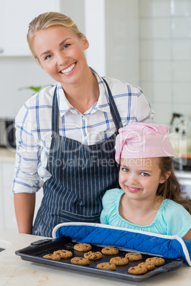 Happy mother and daughter holding tray of baked cookies in kitchen