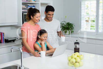 Parents and daughter using laptop in kitchen at home