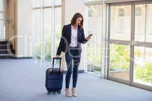 Businesswoman carrying luggage and using mobile phone