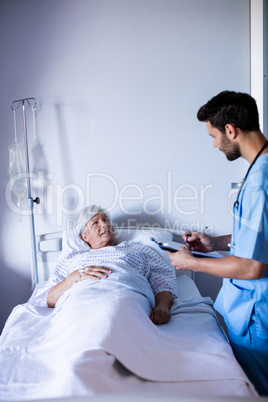 Male doctor discussing medical report with female senior patient on bed