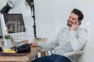 Happy photographer sitting at desk and talking on smartphone