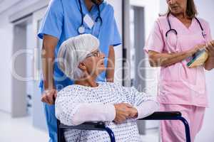 Male and female doctor interacting with female senior patient on wheelchair in corridor