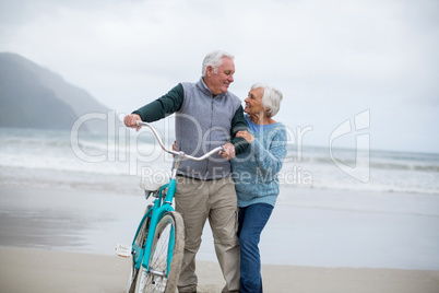 Senior couple standing with bicycle on the beach