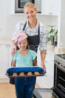 Happy mother and daughter holding tray of baked cookies in kitchen