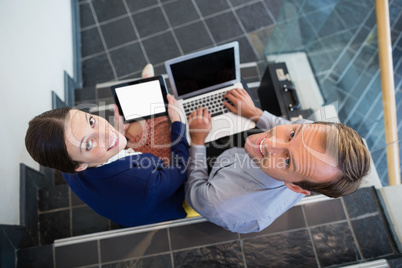 Businessman and woman sitting on steps holding laptop and digital tablet