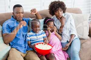 Family and kids watching television while having popcorn in living room