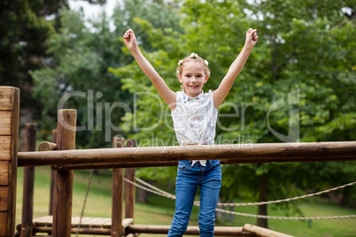 Girl standing with arms up on a playground ride in park