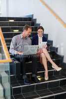 Businessman and woman sitting on steps using laptop