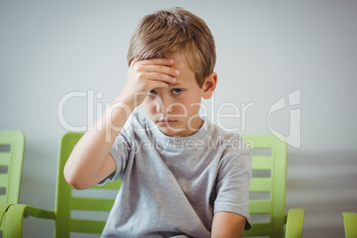 Portrait of upset boy sitting on chair in corridor