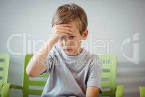Portrait of upset boy sitting on chair in corridor