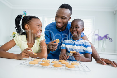 Smiling father and kids eating cookies at home