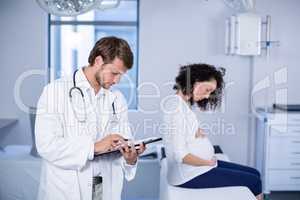 Doctor reading clipboard while examining pregnant woman