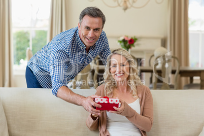 Man surprising woman with a gift in living room