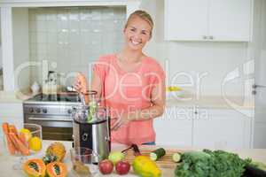 Smiling woman preparing fresh fruit juice in kitchen