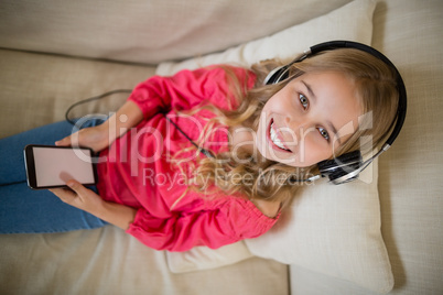 Smiling cute girl listening to music on headphones in living room at home