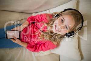 Smiling cute girl listening to music on headphones in living room at home