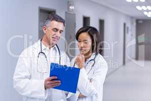 Doctors having discussion on clipboard in corridor