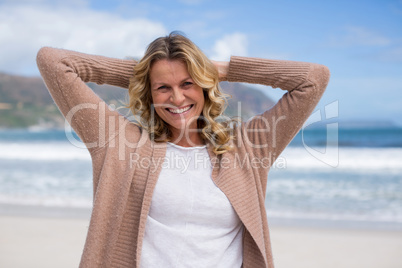 Mature woman with hands behind head standing on the beach