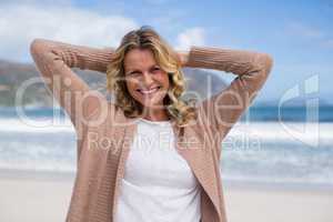 Mature woman with hands behind head standing on the beach