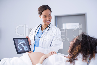 Doctor showing babies ultrasound scan to pregnant woman on digital tablet