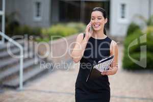 Businesswoman holding clipboard and talking on mobile phone