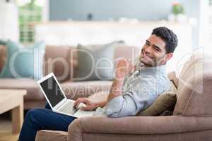 Man sitting on sofa and using laptop in living room at home