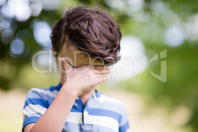 Boy covering eyes with hand in park
