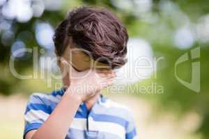 Boy covering eyes with hand in park