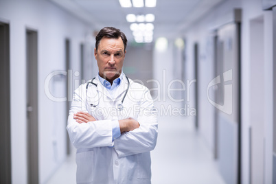 Portrait of male doctor standing with arms crossed in corridor