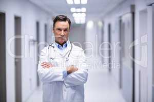 Portrait of male doctor standing with arms crossed in corridor